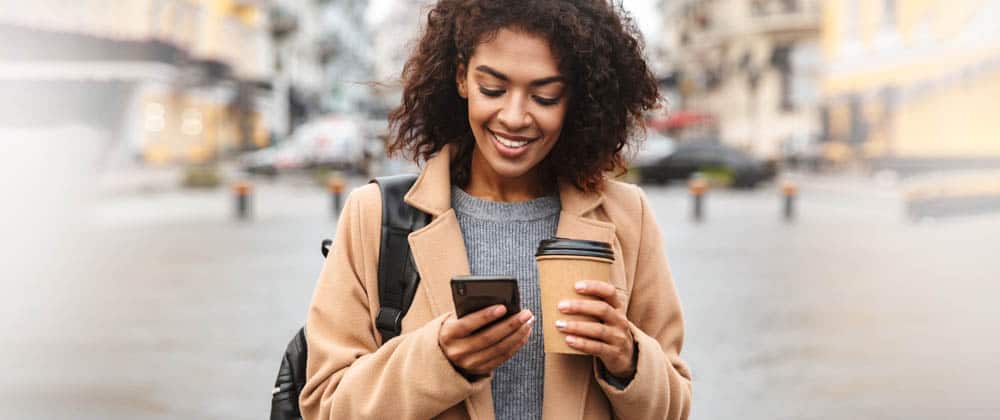 smiling woman holding coffee and looking down at phone