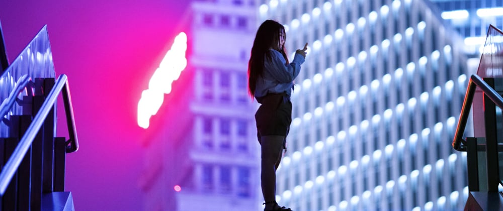 Woman using a phone and standing in front of big neon sign
