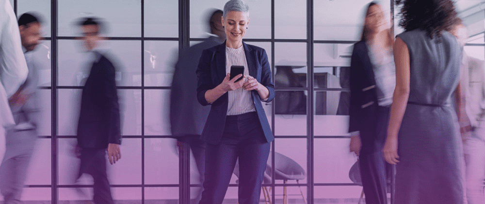 Woman standing in the office looking at her smartphone and smiling