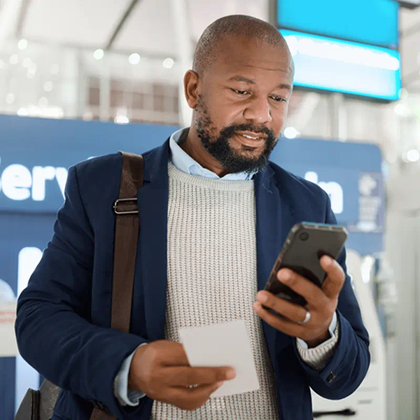 мужчина с бородой и сумкой на плече смотрит в экран мобильного телефона
