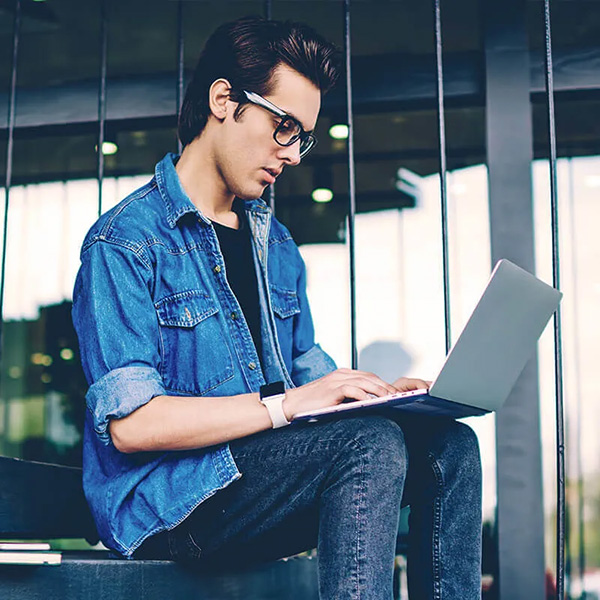 Mann mit Brille sitzt draußen und tippt auf einem Laptop