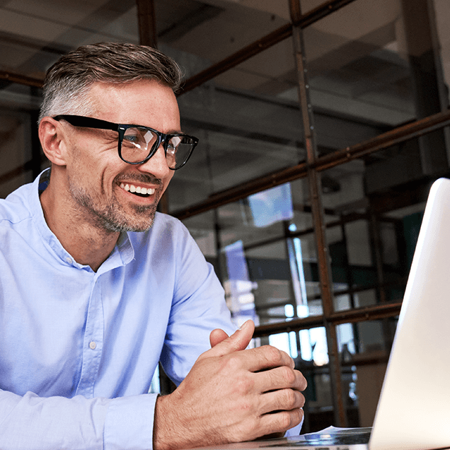 homme portant des lunettes, les mains croisées, souriant devant un ordinateur portable