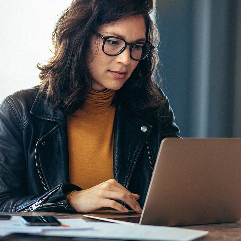 женщина в очках и желтой рубашке смотрит в ноутбук