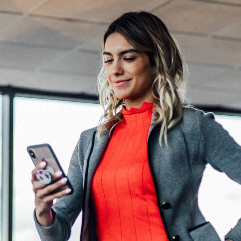 woman with red top smiling down at phone held in hand