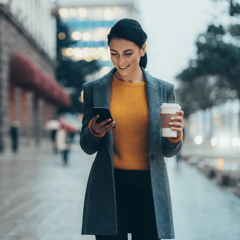 femme portant un haut jaune, qui utilise un téléphone avec un café à la main