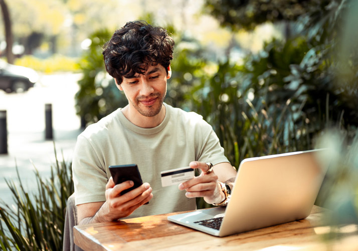 man holding credit card and phone, sitting in front of laptop