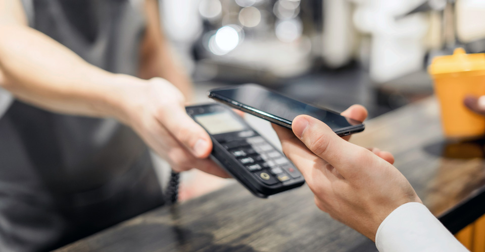Close up photo of man's hand holding a phone and making a NFC payment at a coffee shop