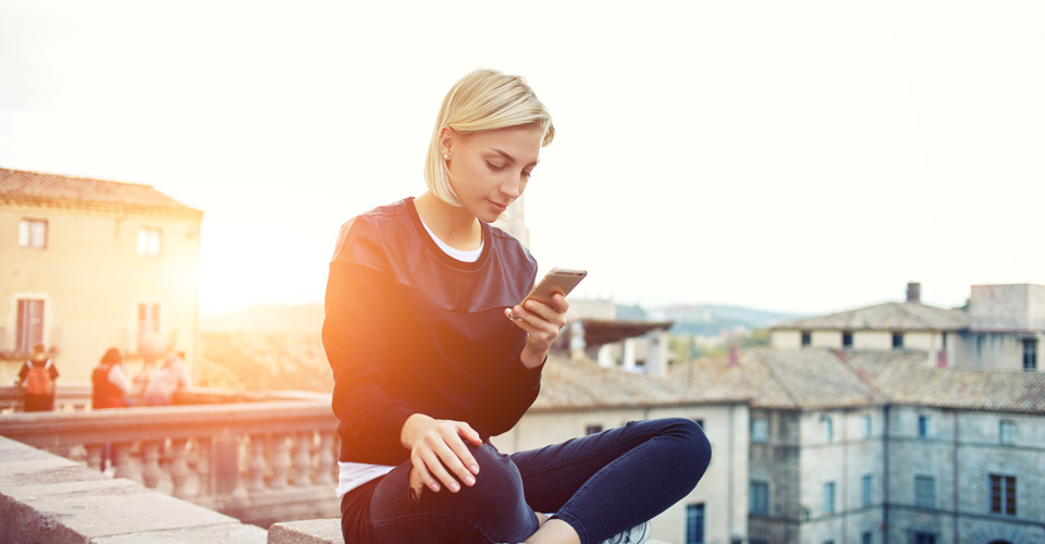 woman sitting with sunset behind her, looking at mobile phone