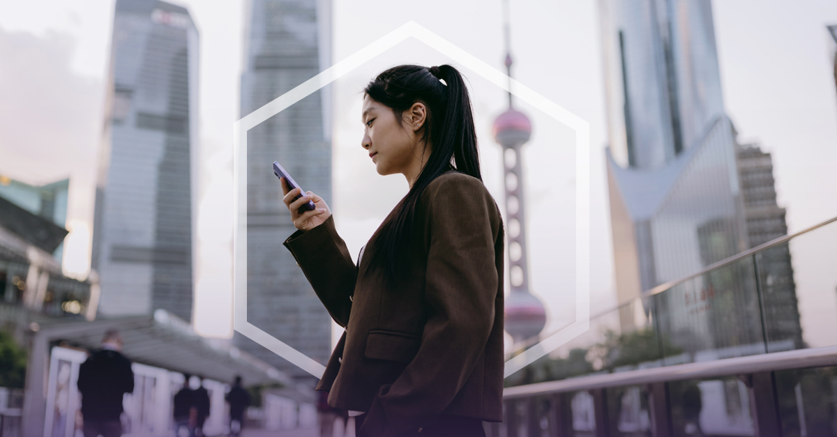 Person using a smartphone in a modern city with tall skyscrapers and the Oriental Pearl Tower in the background