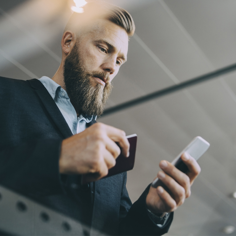 Personne en costume tenant un smartphone et un passeport, debout à l'intérieur sous des plafonniers lumineux.