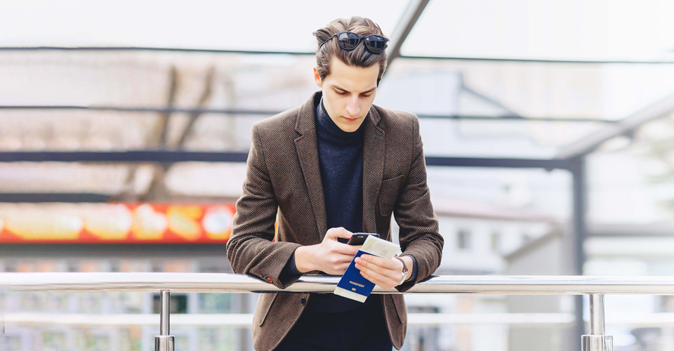 man looking at his mobile phone while holding his passport