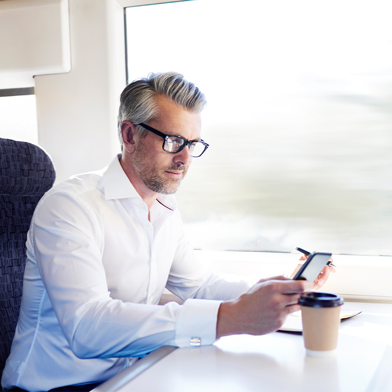 Person in a white shirt sitting on a train, looking at a smartphone with a coffee cup on the table