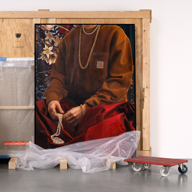 Framed painting of a person in a brown sweatshirt holding a string of pearls, propped against a wooden crate with packing materials nearby