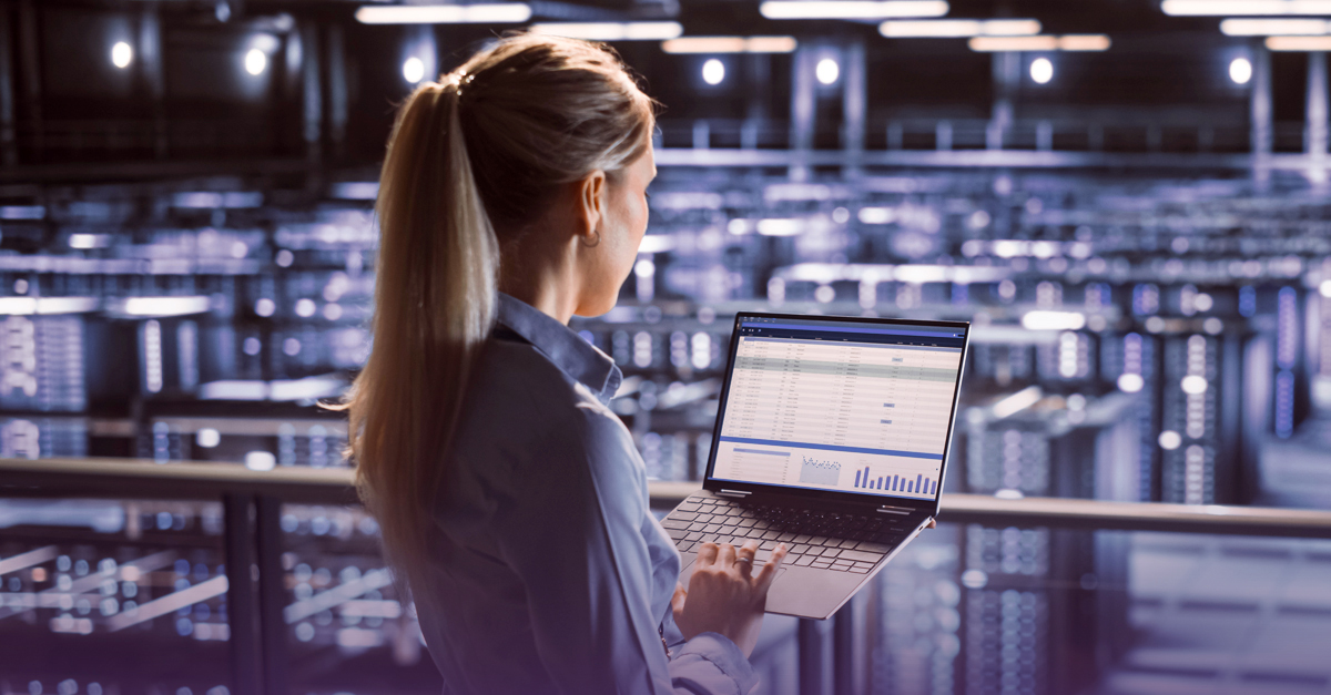 Person using a laptop displaying analytics inside a large data center filled with server racks