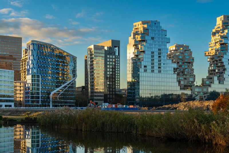 Modern glass high‑rise buildings reflected in a waterfront canal at sunset