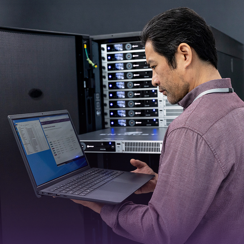 Person using a laptop in a server room with rack-mounted equipment