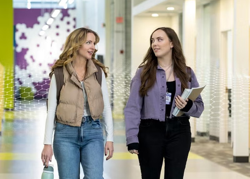 Two people walking together down a brightly lit hallway, carrying a water bottle and folders