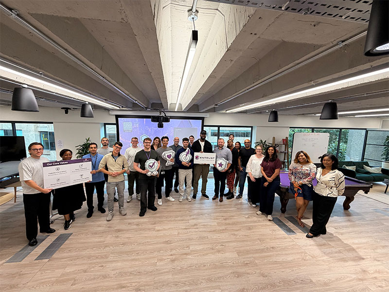 Group photo of employees standing in an office, holding company awards and recognition signs
