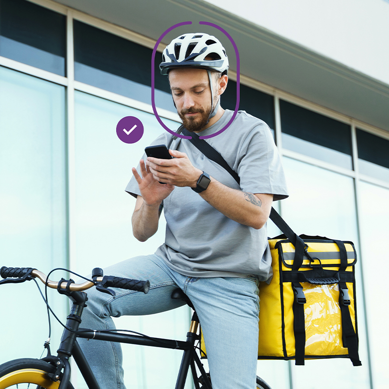 Delivery cyclist using a smartphone, with facial verification highlighted on screen