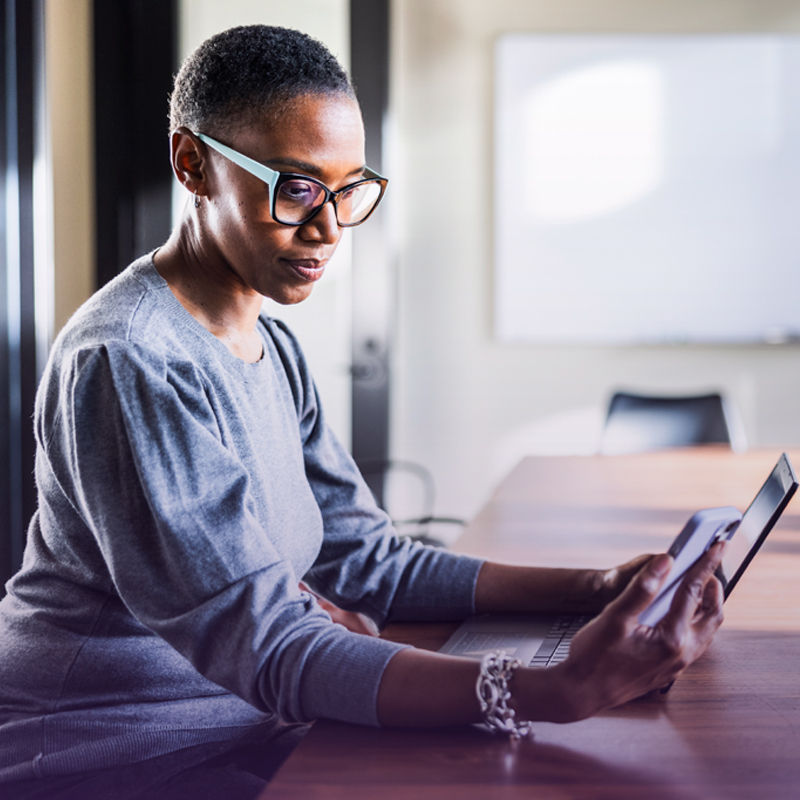Person sitting at a table, using a smartphone beside a laptop