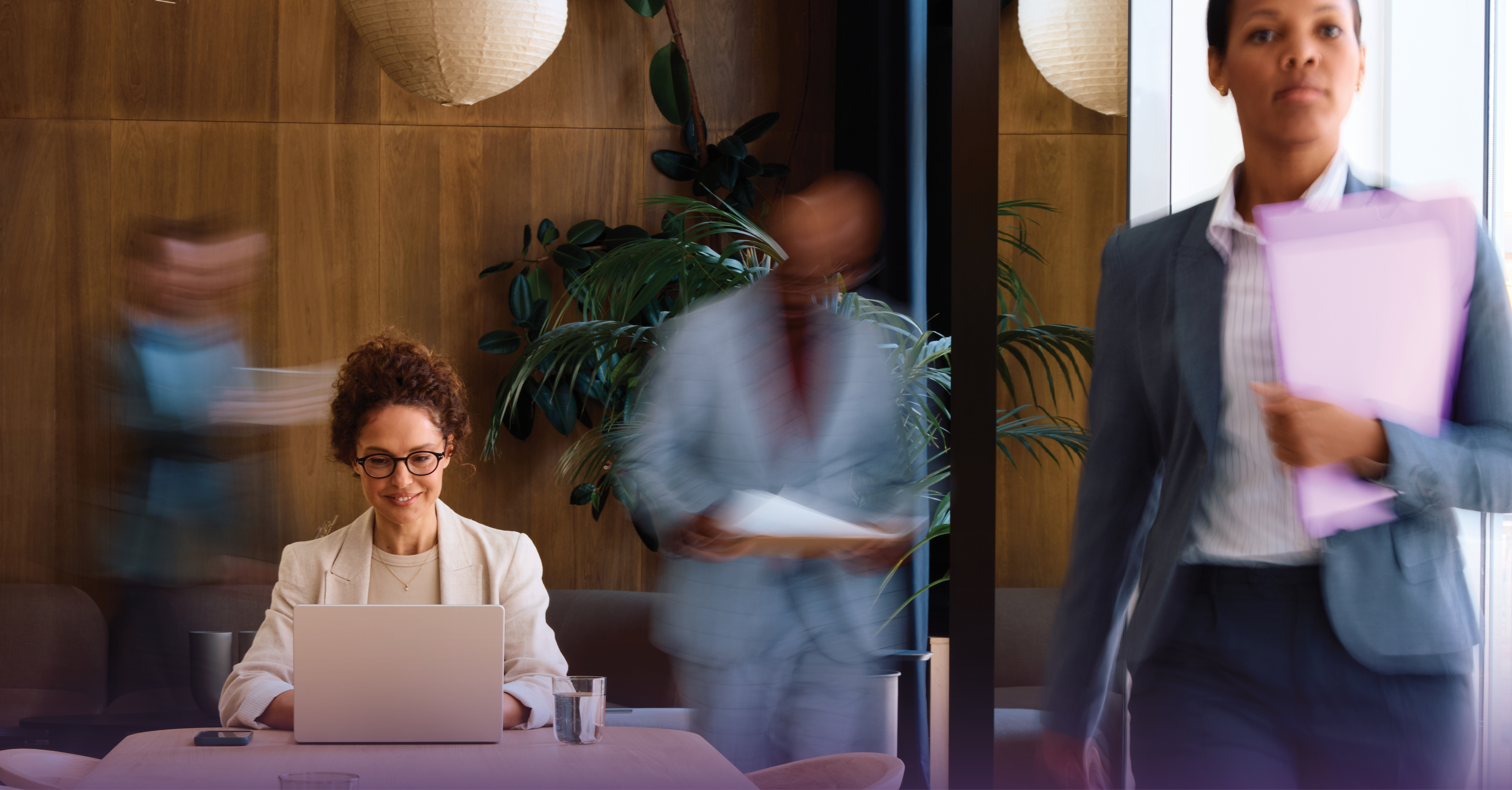 Person working on a laptop in a busy office while coworkers move past
