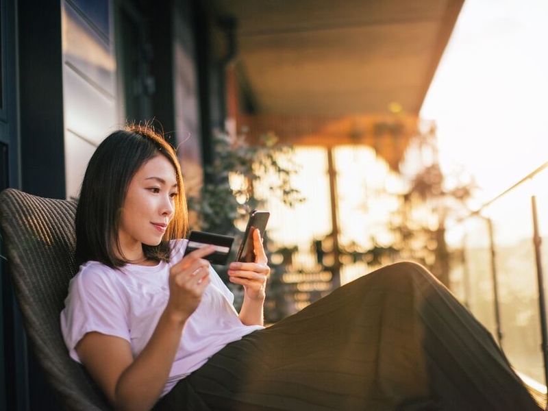 Person sitting on a patio holding a phone and a credit card