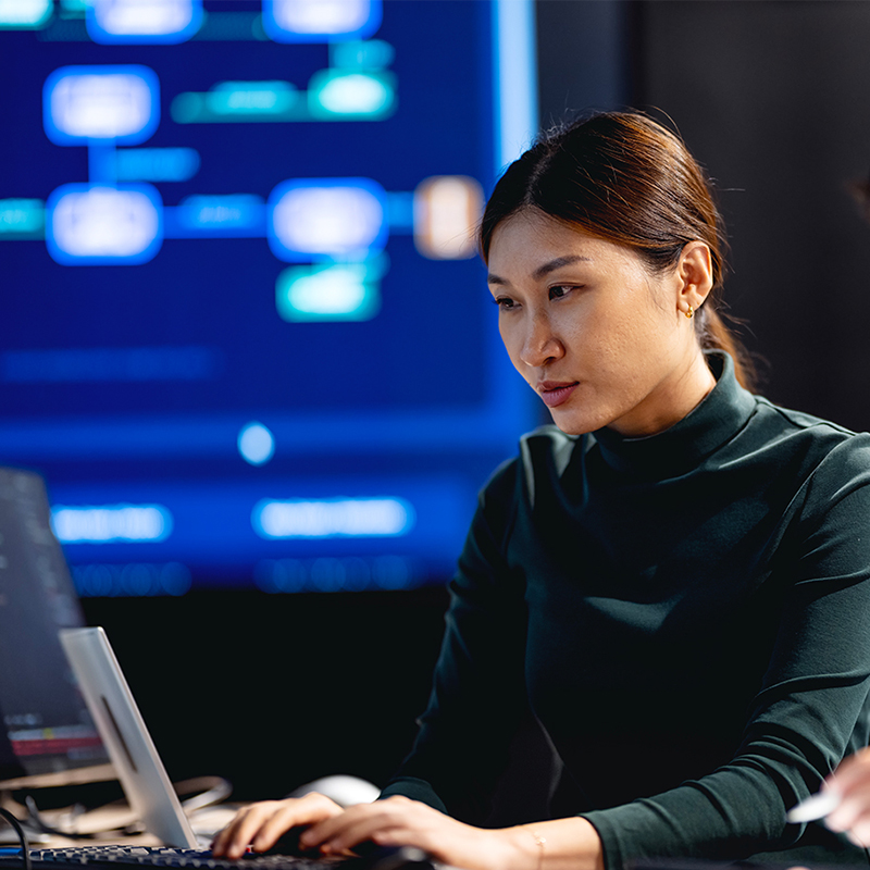 Person working at a computer with digital workflow and data visualization screens in the background