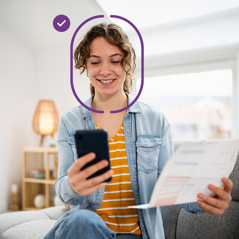 Person holding a smartphone and document while completing facial identity verification on a mobile device
