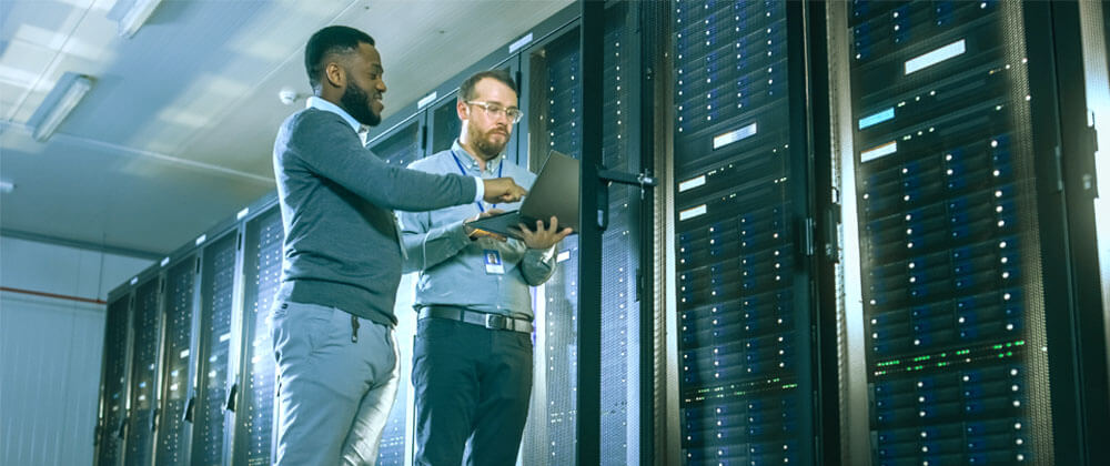 Two men looking at a laptop in a server room